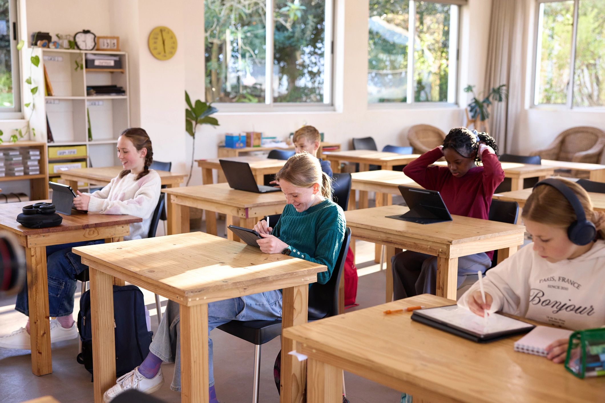 Students working independently with tablets and notebooks in a bright classroom